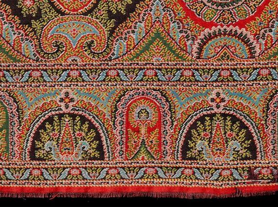 Paisley shawl pattern, short length of a woven border with long cone or buta shapes at the centre, detailed multi-coloured design predominantly in shades of red, blue and green.